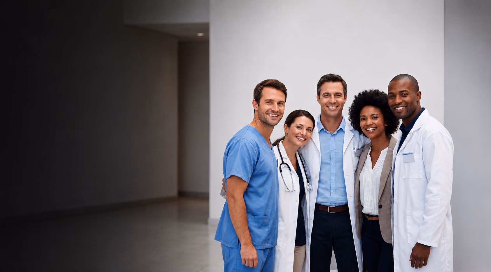 Cinco profissionais da saúde sorrindo em um corredor hospitalar amplo e iluminado, com grande espaço negativo na parte superior da imagem